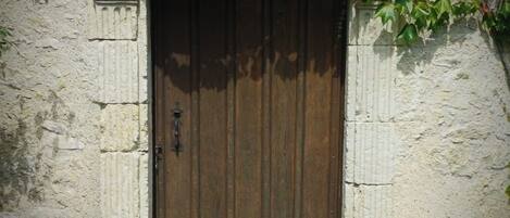 A rustic wooden door with a metal handle, set in a stone wall with a small step leading up to it.