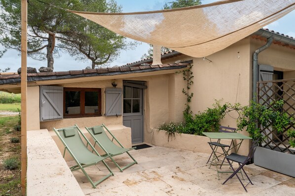Eine Terrasse mit zwei Lounge-Stühlen und einem Tisch, einer Tür und einem überdachten Bereich mit Sonnenschutz.