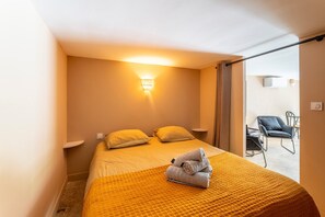 A hotel room with a bed, a wall-mounted light, a chair, and a view through a sliding door. - Maison Marvic en Provence with Private Pool, Mountain Views, and Vineyards (Apt)