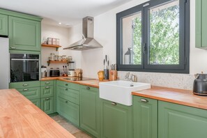 A kitchen with green cabinets, a stainless steel range hood, a window with a view of greenery, and a white sink. - Maison Marvic en Provence with Private Pool, Mountain Views, and Vineyards (Apt)