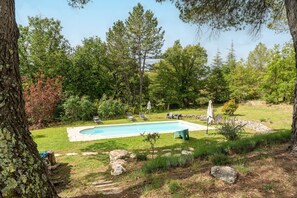 A swimming pool surrounded by a grassy area with trees, a stone wall, and outdoor seating. - Maison Marvic en Provence with Private Pool, Mountain Views, and Vineyards (Apt)