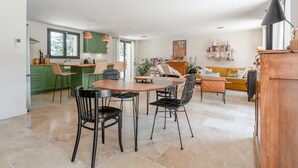 Eine moderne Küche mit grünen Schränken, ein Essbereich mit Holztisch und -stühlen sowie ein Wohnzimmer mit Sofa und Couchtisch.
