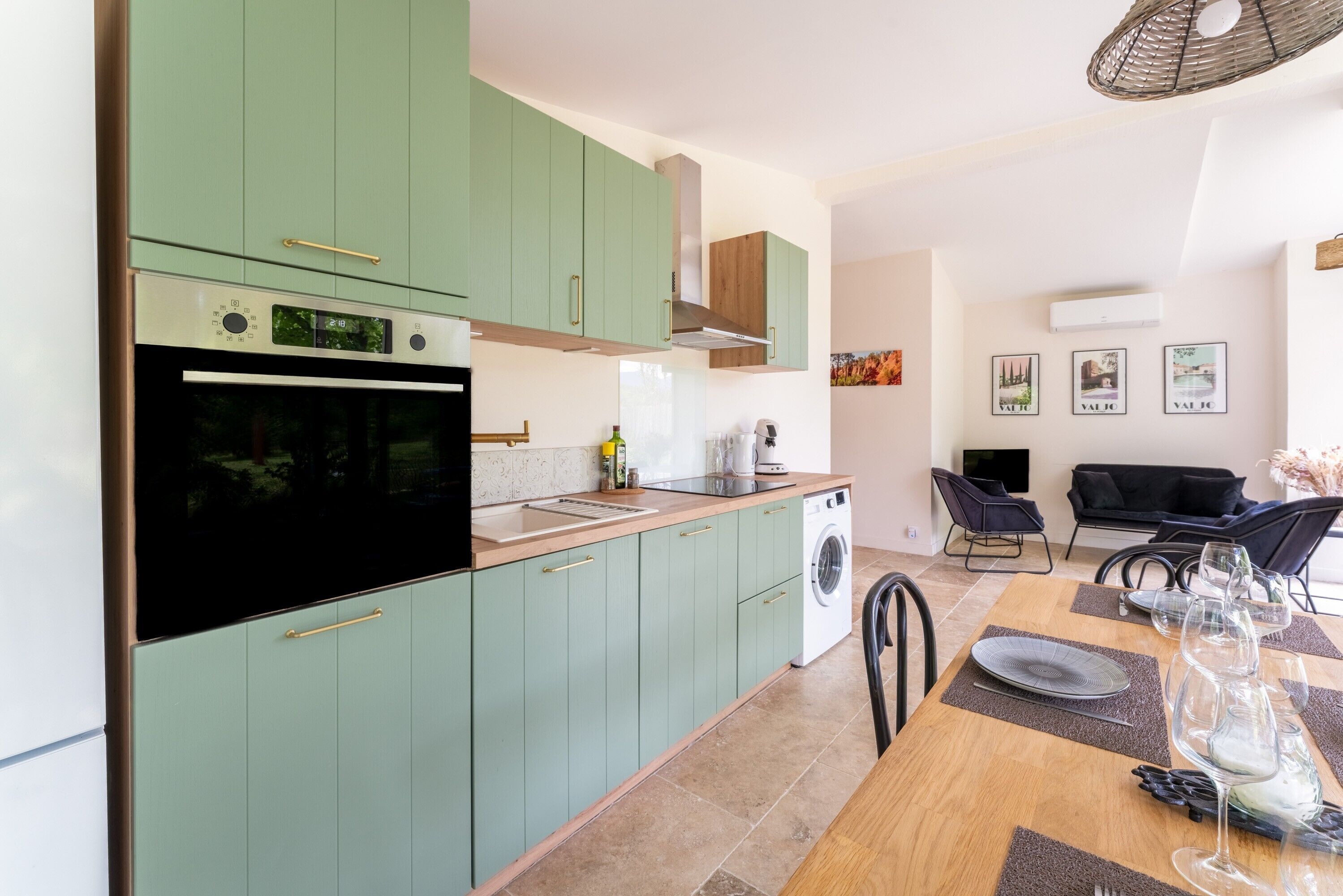 Une cuisine moderne avec des meubles de couleur verte, un four encastré et un coin repas avec une table dressée pour quatre personnes.