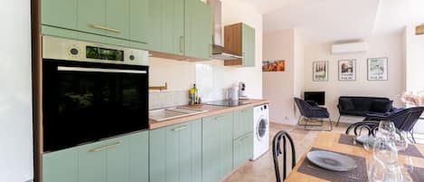 Une cuisine moderne avec des meubles de couleur verte, un four encastré et un coin repas avec une table dressée pour quatre personnes.