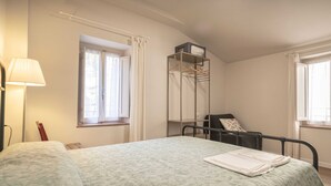 Un dormitorio con cama, mesita de noche, lámpara, ventana con cortinas, armario y una silla.