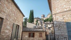 Una calle estrecha con edificios de piedra, un árbol alto y una torre al fondo.