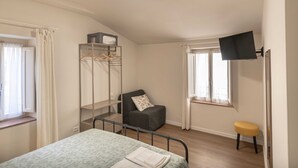 Un dormitorio con cama, una silla, televisor, armario y ventana.