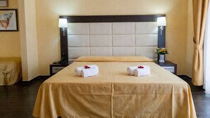 Habitación de hotel con una cama grande, dos mesitas de noche, una lámpara y un florero con flores.