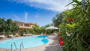 A swimming pool with sun loungers and a covered seating area, surrounded by greenery and a building in the background. - Hotiday Tropea Parghelia (Parghelia)