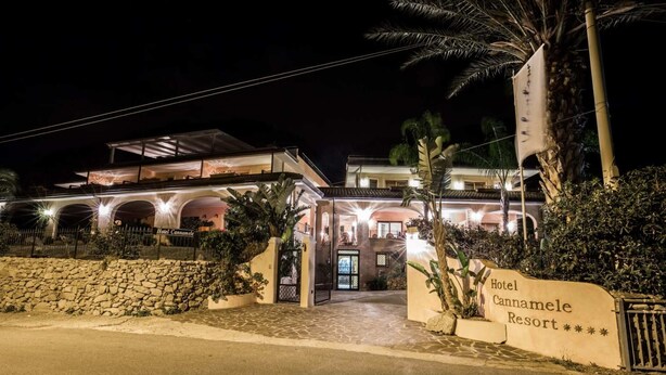 A hotel entrance with a stone wall, palm trees, and a sign for Hotel Cannamele Resort. - Hotiday Tropea Parghelia (Parghelia)