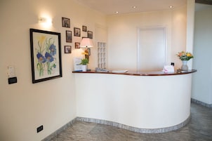 Un mostrador de recepción con una encimera blanca, obras de arte en la pared, una lámpara y un jarrón con flores.