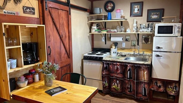 Een kleine keuken met een houten tafel, een bordje met koffie, een kookplaat, een magnetron en een koelkast.