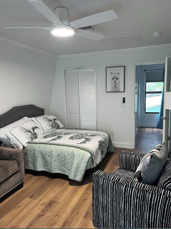 A bedroom with a bed, a chair, a ceiling fan, and a door leading to another room.