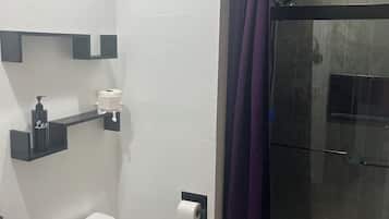 A bathroom with a toilet, a glass shower enclosure, and a shelf with toiletries.