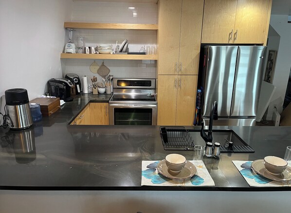 A modern kitchen with stainless steel appliances, wooden cabinets, and a black countertop.