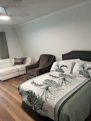 A bedroom with a bed, a chair, a sofa, and a ceiling fan.