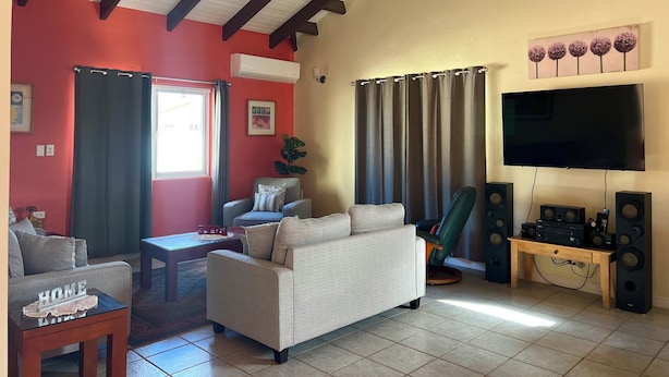 A living room with a sofa, a coffee table, a TV, and a sound system. - Villa Emilia  (Oranjestad)