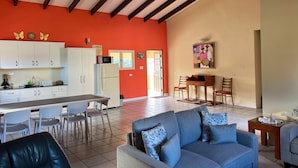 A spacious living area with a sofa, dining table, chairs, and a kitchen with cabinets and appliances. - Villa Emilia  (Oranjestad)