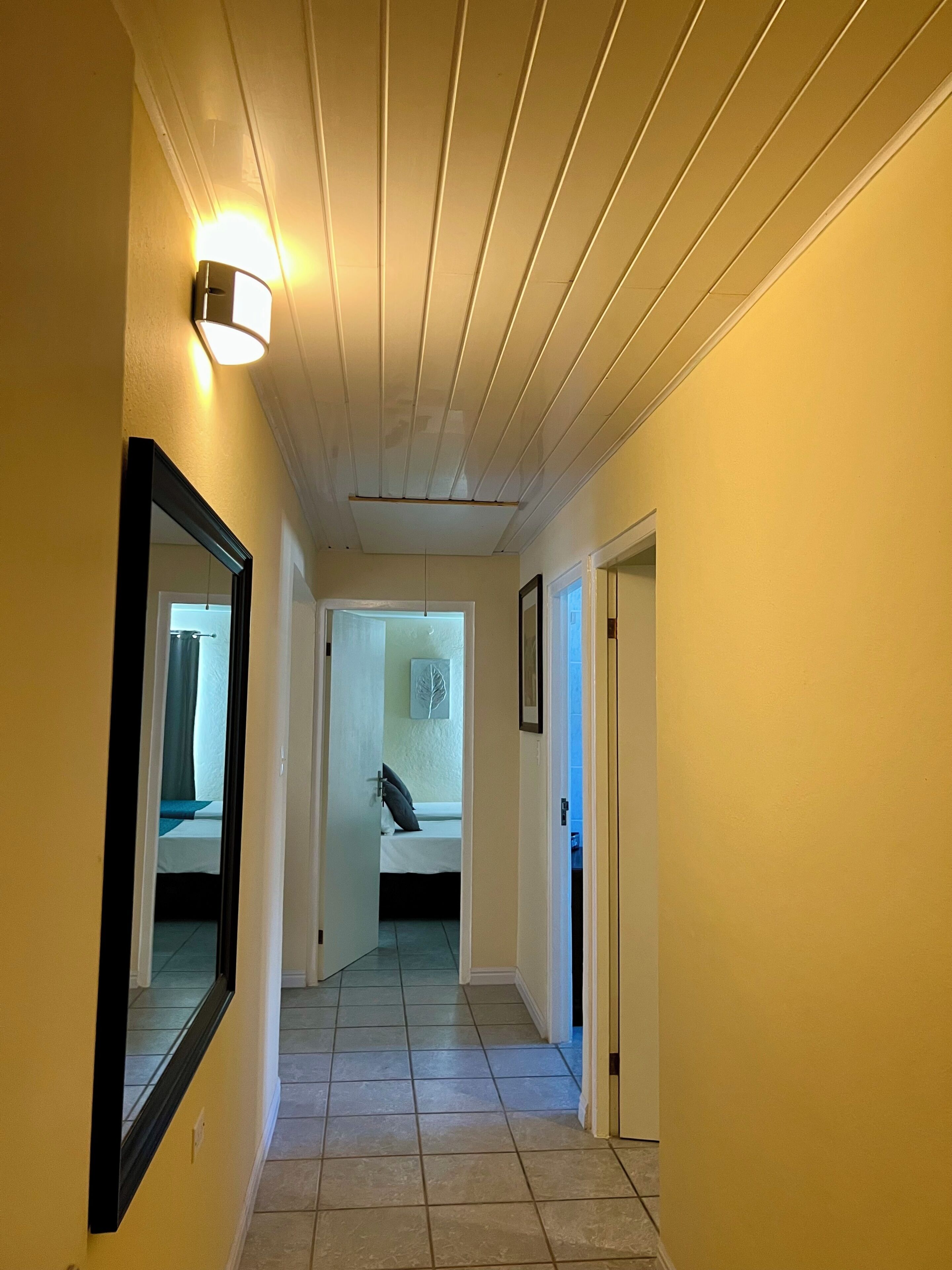 Ein Flur mit einem Bett im Hintergrund, einer Tür rechts und einer Leuchte links.