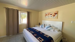 A bedroom with a bed, curtains, a window, a painting, and a tiled floor. - Villa Emilia  (Oranjestad)