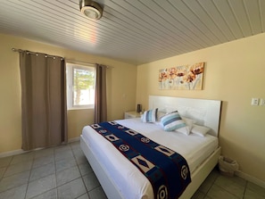 A bedroom with a bed, curtains, a window, a painting, and a tiled floor. - Villa Emilia  (Oranjestad)