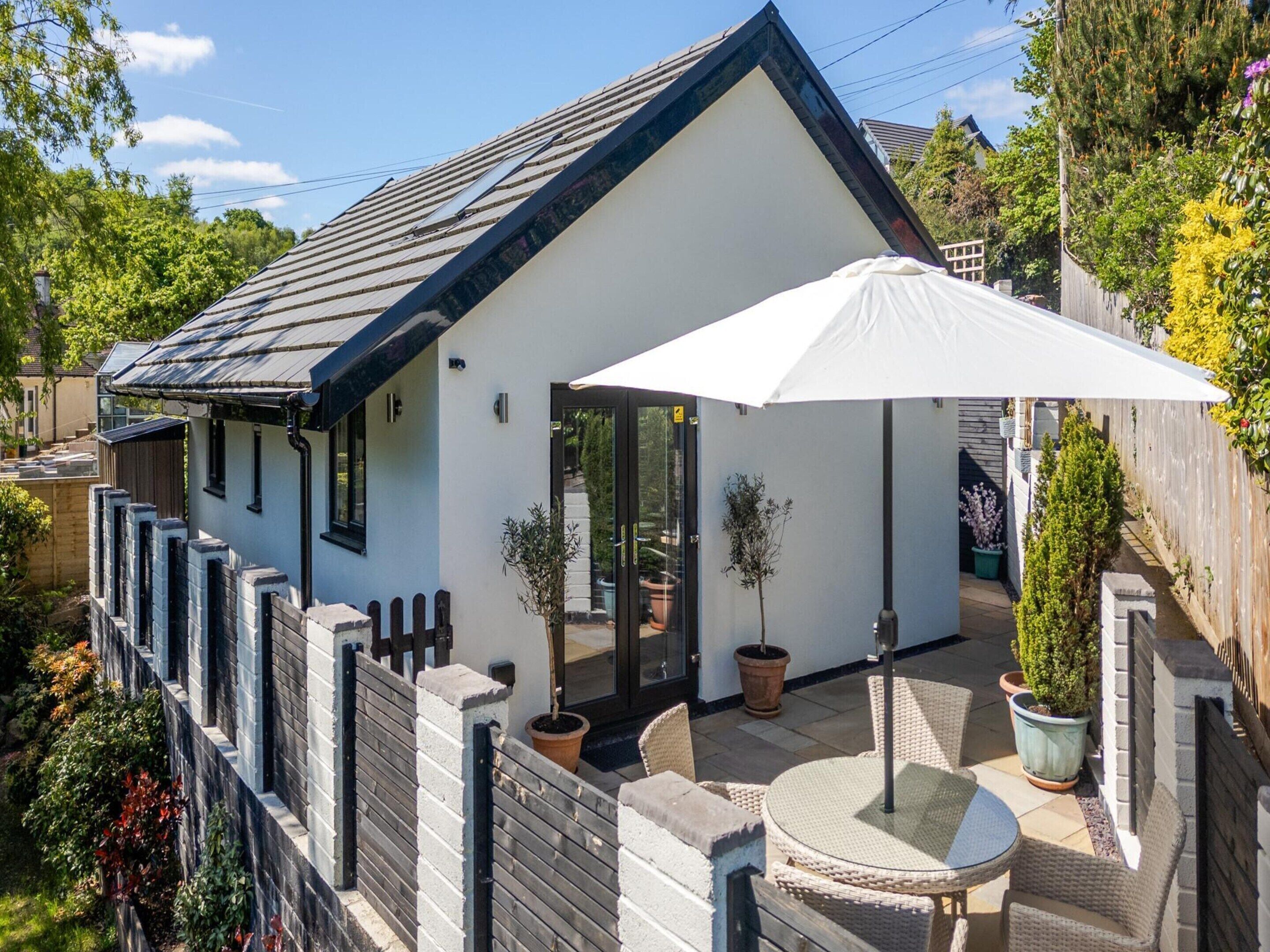 A white house with a black roof, a wooden fence, and a patio with chairs and a table.