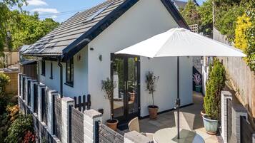 A white house with a black roof, a wooden fence, and a patio with chairs and a table.