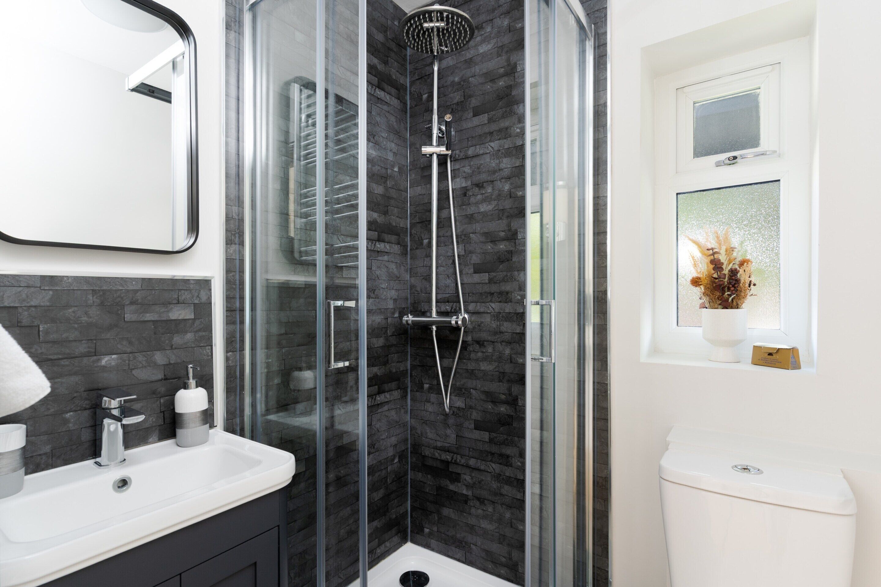 A modern bathroom with a glass-enclosed shower, a white sink, and a toilet.