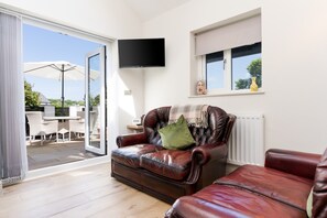 A living room with a leather sofa, a television mounted on the wall, and a sliding glass door leading to an outdoor patio area. - South Wales Lodge With Patio (Newport)