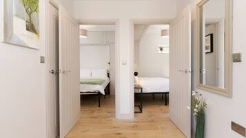 A hallway leading to two bedrooms with wooden flooring, white walls, and a mirror on the right.