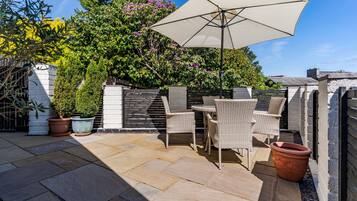 A patio with outdoor furniture, a large umbrella, and potted plants.