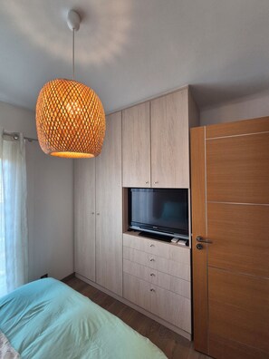 A bedroom with a bed, a wardrobe, a television, and a hanging light fixture. - New, bright 2-room apartment with ocean views and direct access to the beaches, near Menton and Monaco (Roquebrune-Cap-Martin)