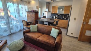A living room with a brown leather sofa, a round knitted ottoman, and a dining area with a table and chairs. - New, bright 2-room apartment with ocean views and direct access to the beaches, near Menton and Monaco (Roquebrune-Cap-Martin)