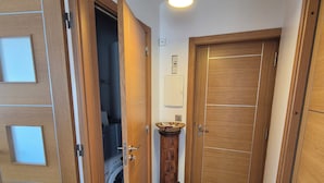 A hallway with a wooden door, a washing machine, and a pendant light. - New, bright 2-room apartment with ocean views and direct access to the beaches, near Menton and Monaco (Roquebrune-Cap-Martin)