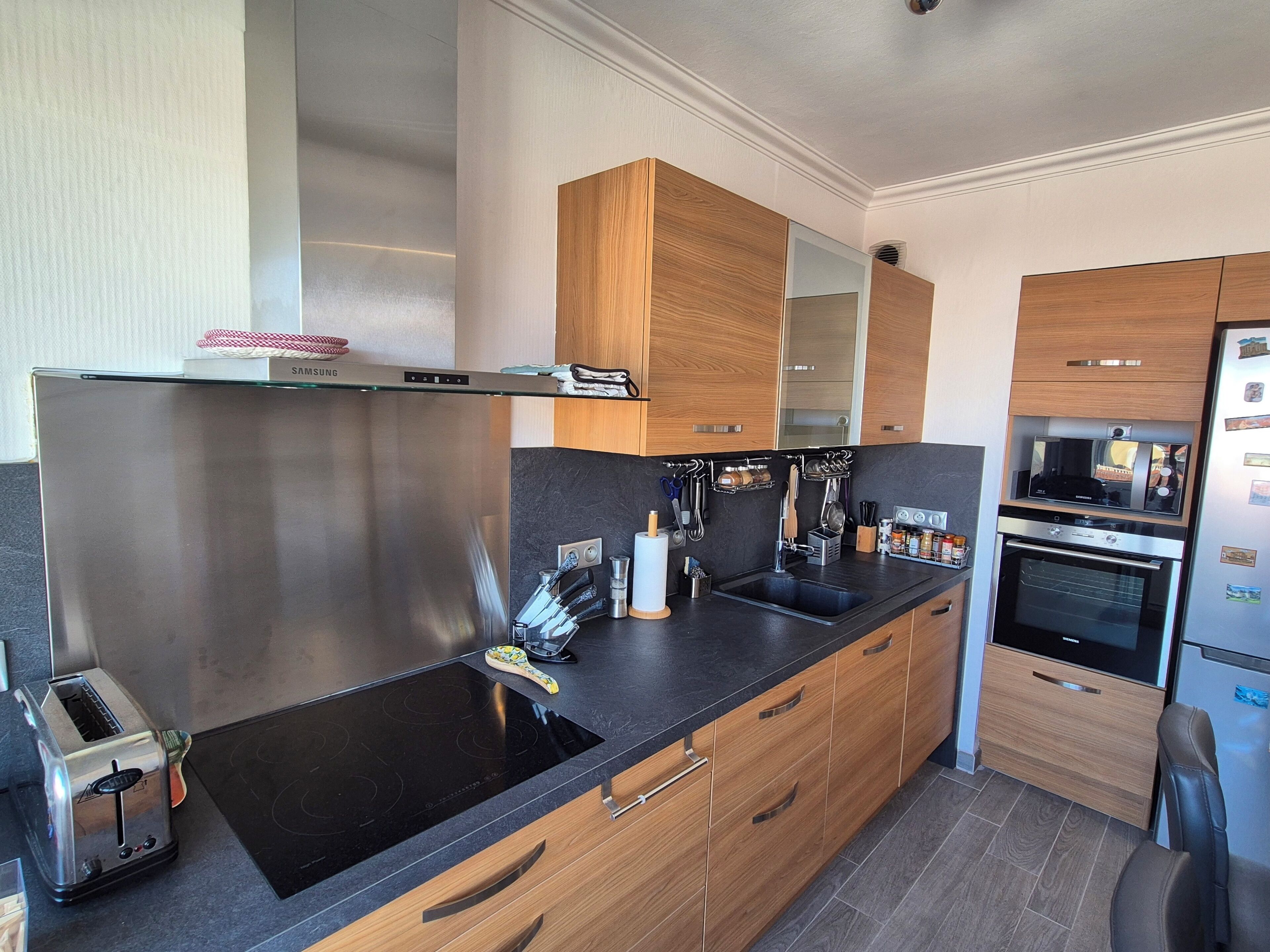 A modern kitchen with stainless steel appliances, wooden cabinets, and a black countertop.