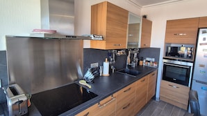 A modern kitchen with stainless steel appliances, wooden cabinets, and a black countertop. - New, bright 2-room apartment with ocean views and direct access to the beaches, near Menton and Monaco (Roquebrune-Cap-Martin)