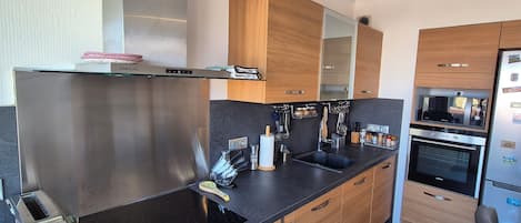 A modern kitchen with stainless steel appliances, wooden cabinets, and a black countertop.