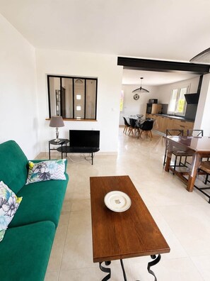 A living room with a green sofa, a wooden coffee table, a TV, and a dining area with chairs and a table. - "La Parenthèse de Caminade" on the outskirts of Sarlat (Sarlat-la-Canéda)