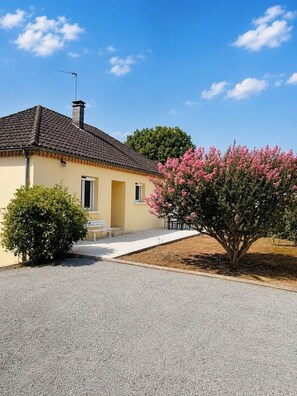 Ein eingeschossiges Haus mit Ziegeldach, einer kleinen Veranda und einem Schotterweg.