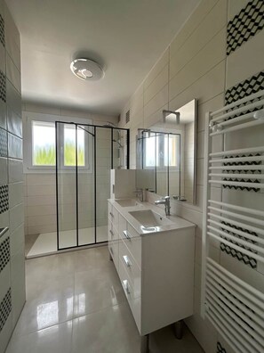 Ein modernes Badezimmer mit Duschkabine aus Glas, einem weißen Waschtisch mit Spiegel und einem Handtuchhalter.