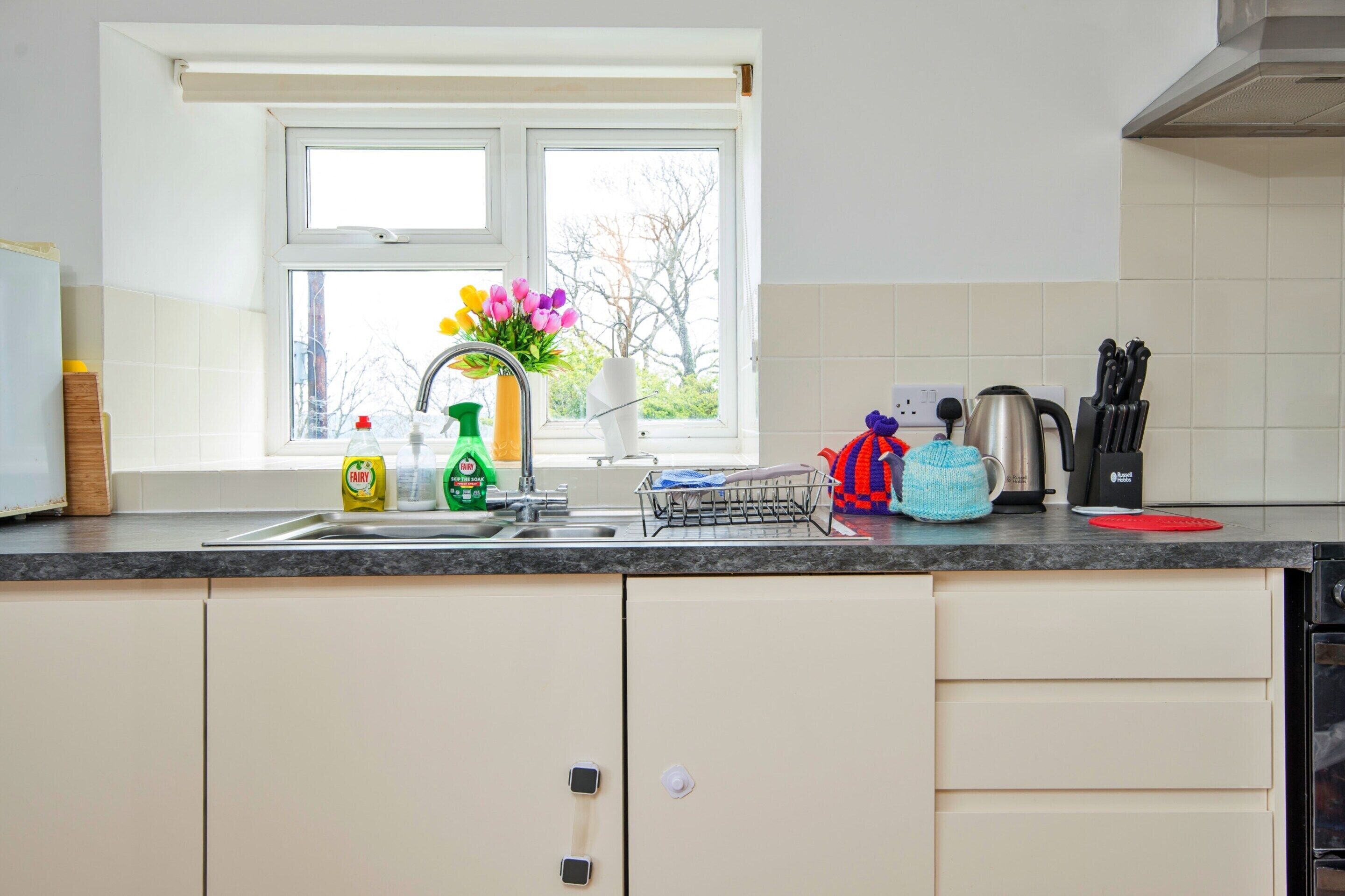 Eine Küche mit Fenster, Spüle, Wasserkocher und verschiedenen Küchenutensilien.