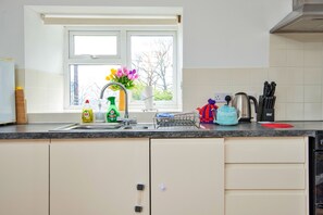 Eine Küche mit Fenster, Spüle, Wasserkocher und verschiedenen Küchenutensilien.