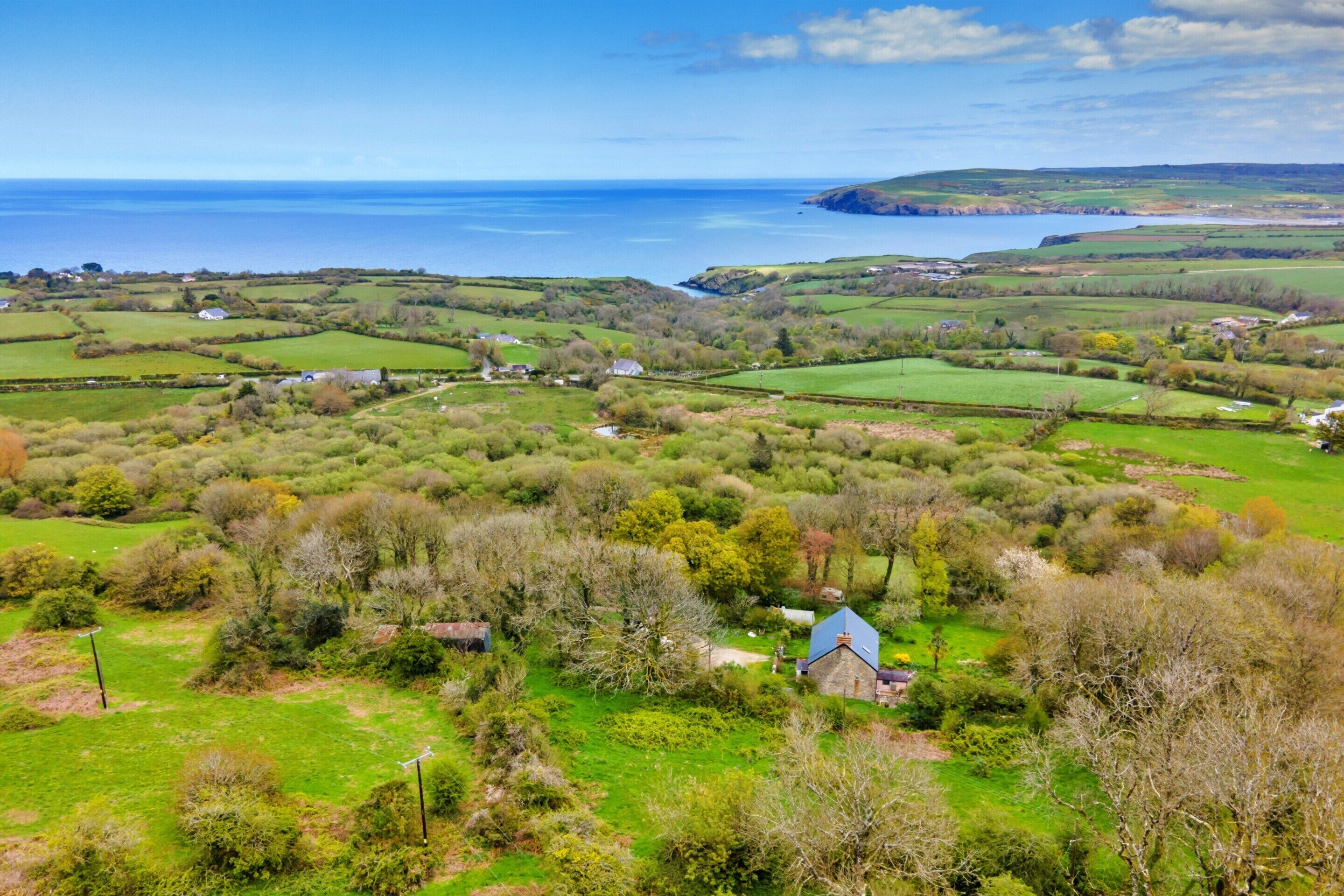 A rural landscape with rolling hills, a small house with a blue roof, and a view of the sea.