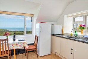 A kitchen with a view of the sea, a refrigerator, a sink, and a dining table with chairs. - Charming Snowdonia Slate Cottage (Newport)