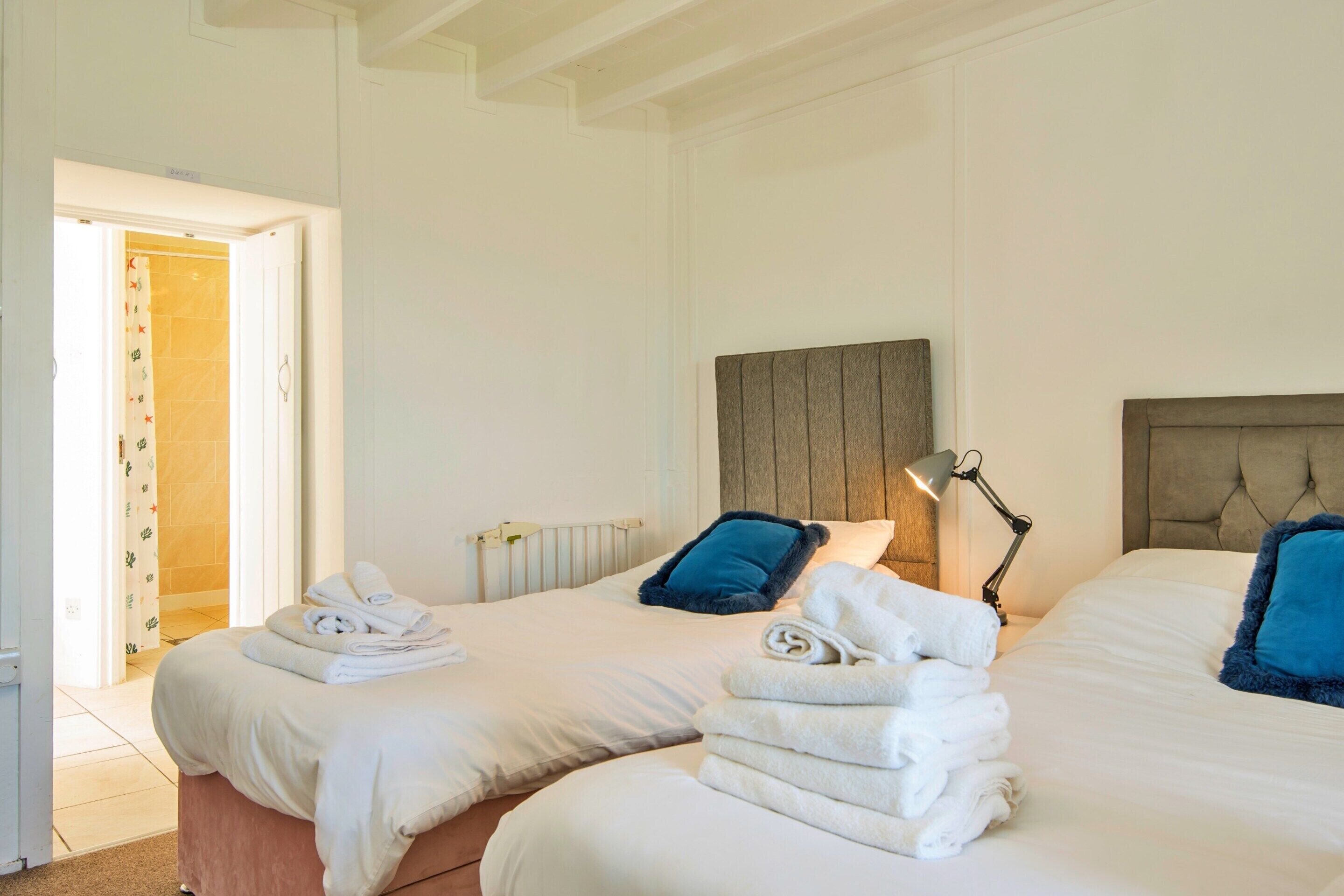 A hotel room with two beds, a radiator, a lamp, and a door leading to a bathroom.