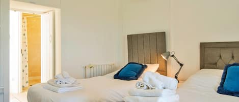 A hotel room with two beds, a radiator, a lamp, and a door leading to a bathroom.