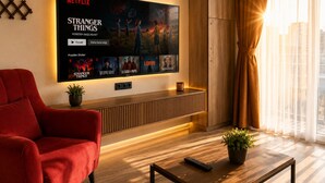 En moderne stue med et stort fladskærms-tv på væggen, en rød sofa, et træ sofabord og en potteplante.