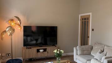 A living room with a flat-screen TV, a sofa, a coffee table, and a floor lamp.