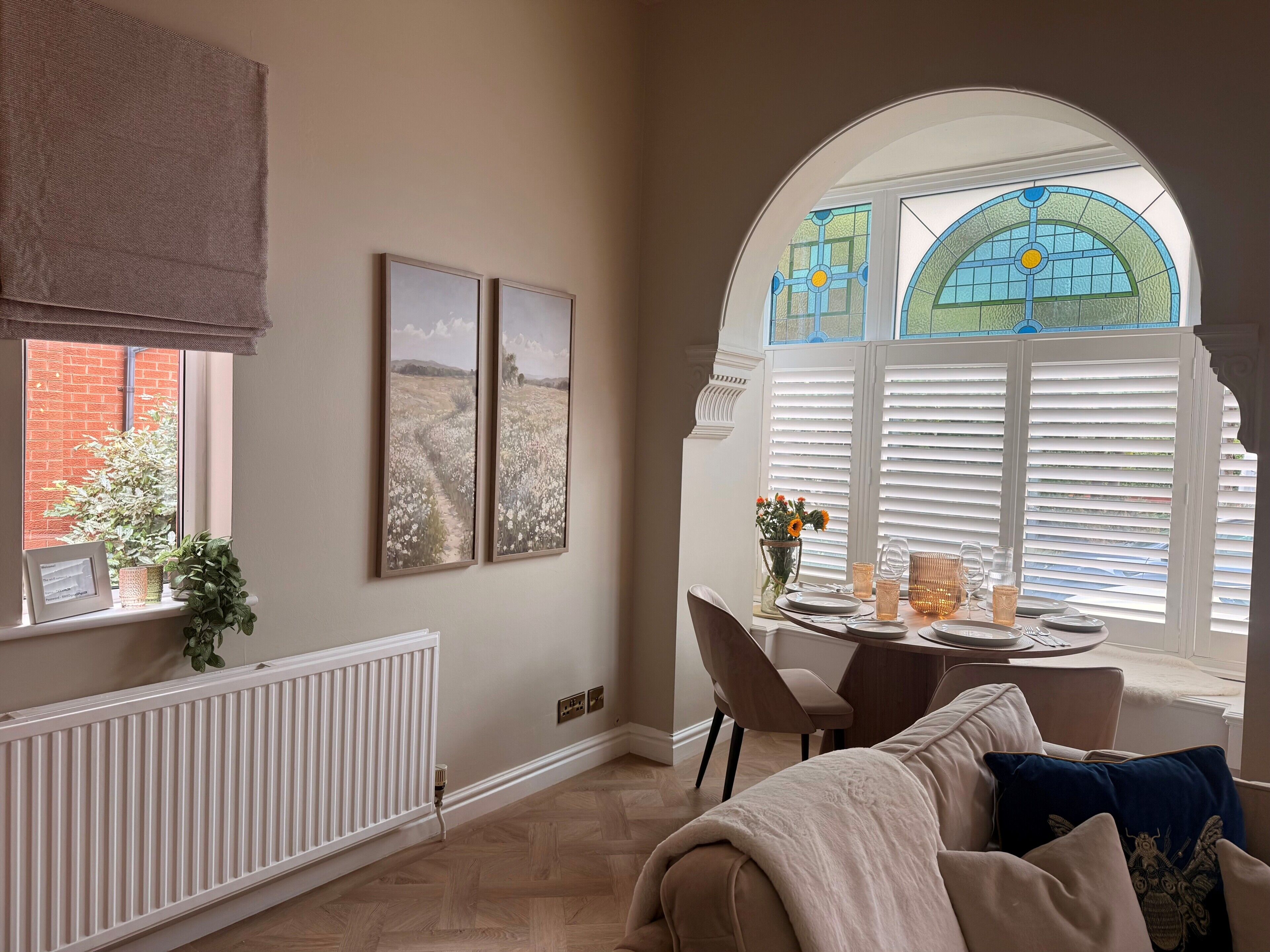 A room with a radiator, a table set for dining, a sofa, and a window with blinds.