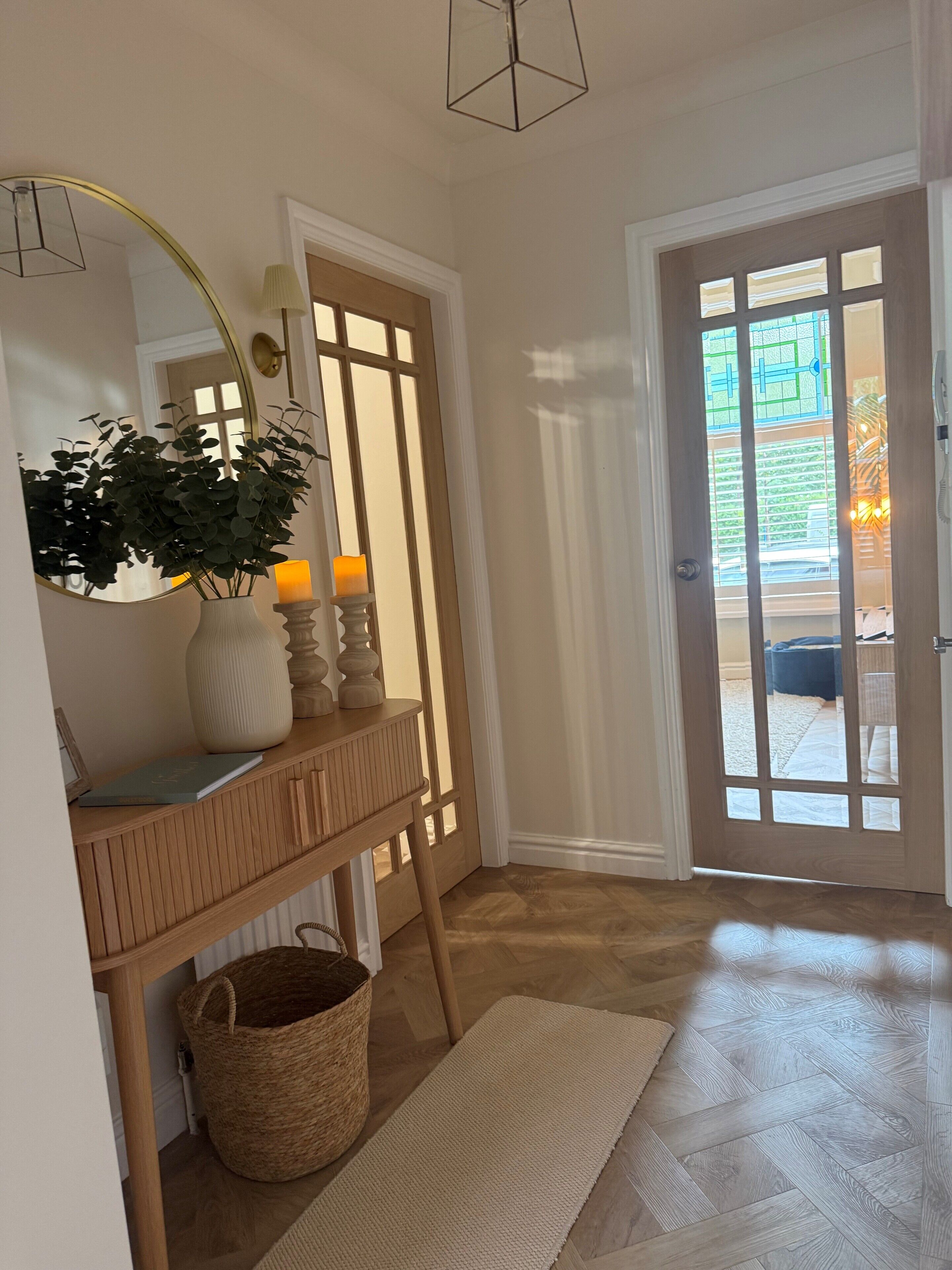 A hallway with a wooden bench, a mirror, a vase with a plant, a candle, and a door with glass panels.
